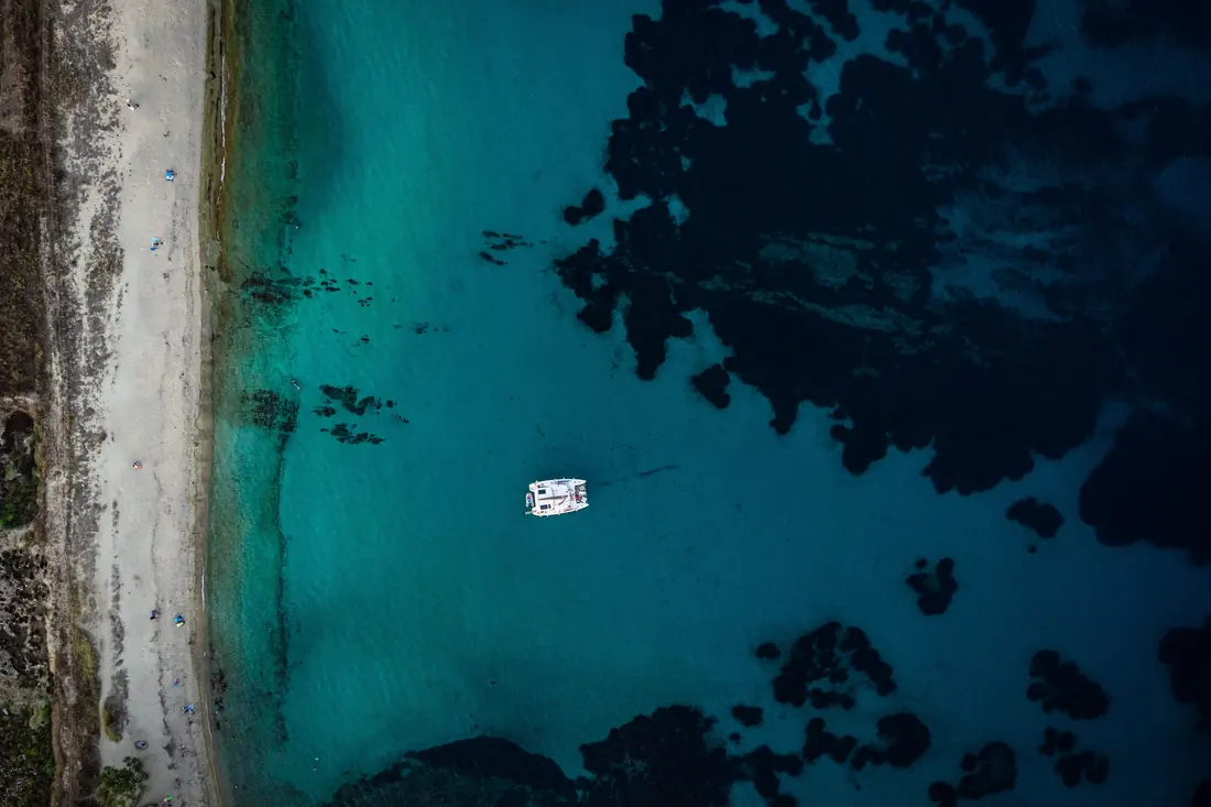 Overhead aerial view of the coast at Nikiti: a pale strip of sand, shallow turquoise water and a white catamaran