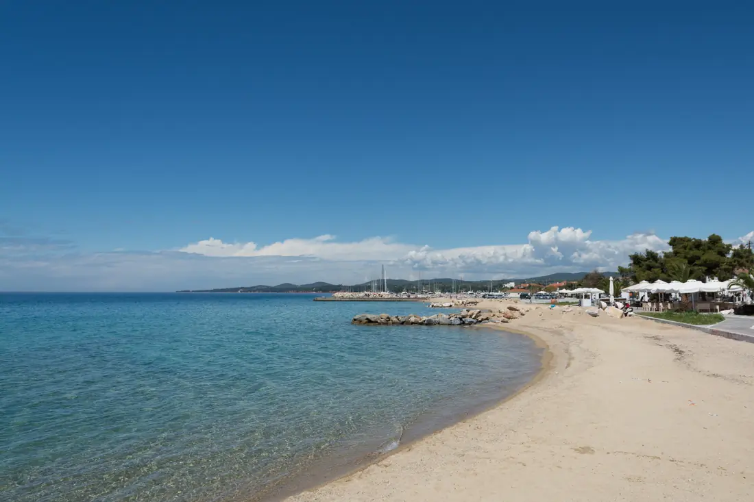 The sandy beach at Nikiti with shallow water, the marina and the village beach bars behind